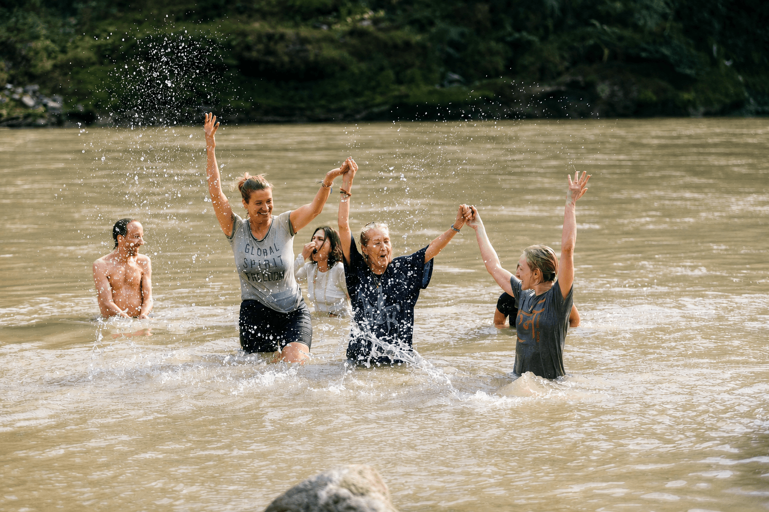 A group celebrating together in a river, arms raised in joy