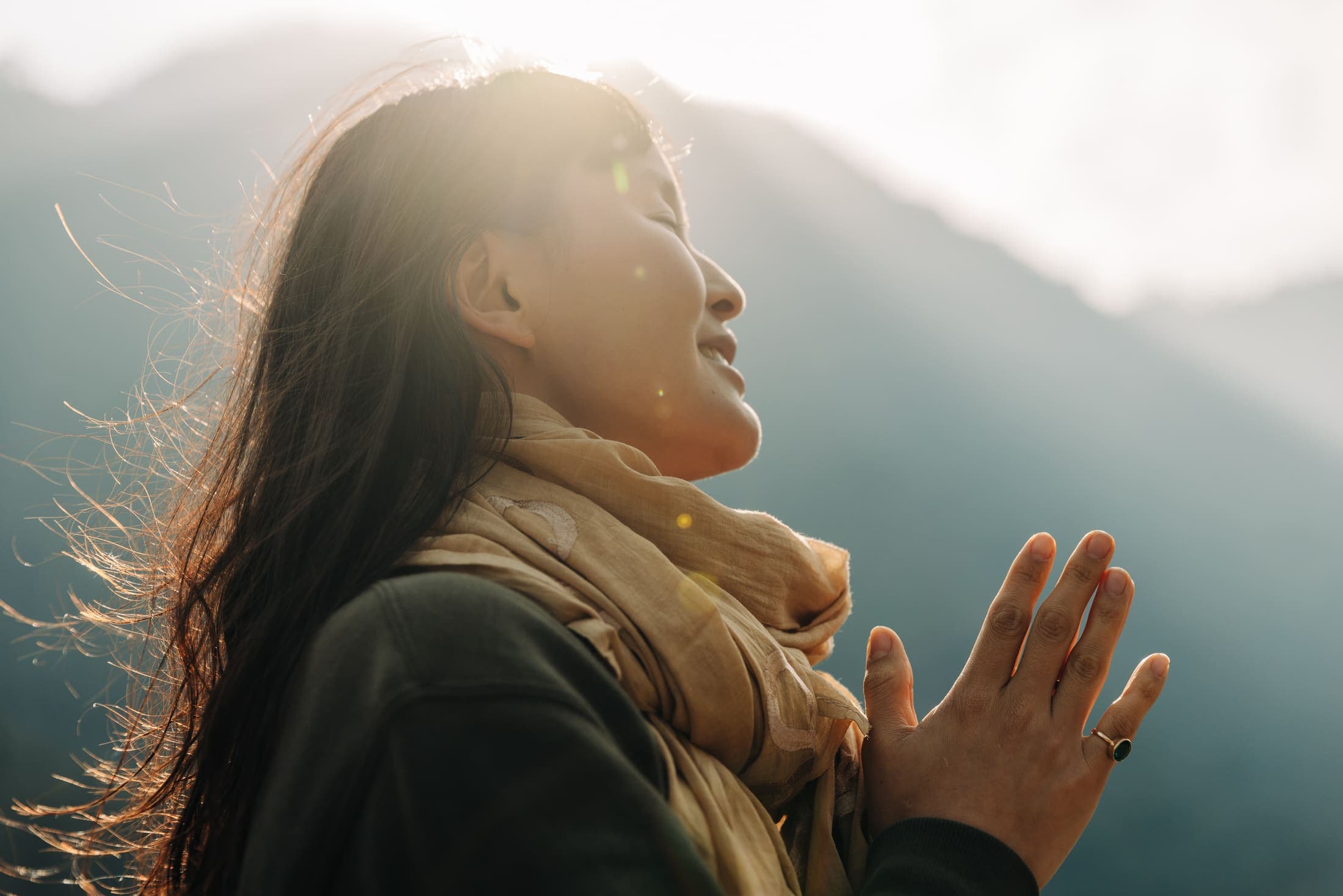 Woman in prayer pose, backlit by sunlight with mountains in the background