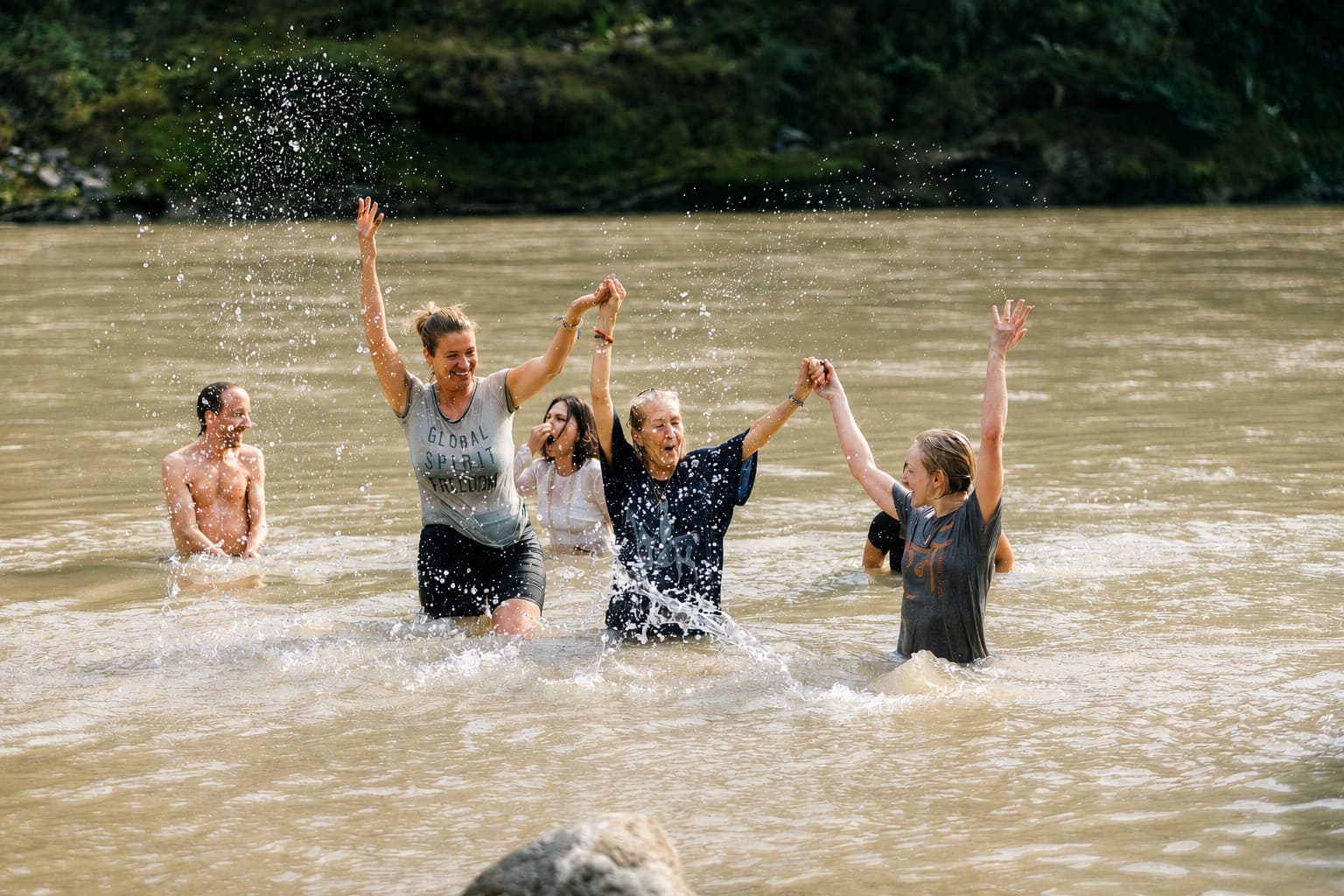 A group of friends celebrating together in a river, arms raised and hands joined in joy