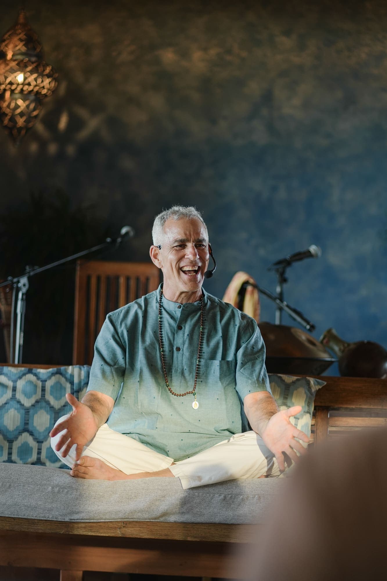 A retreat facilitator laughing warmly mid-conversation, mala necklace, seated cross-legged